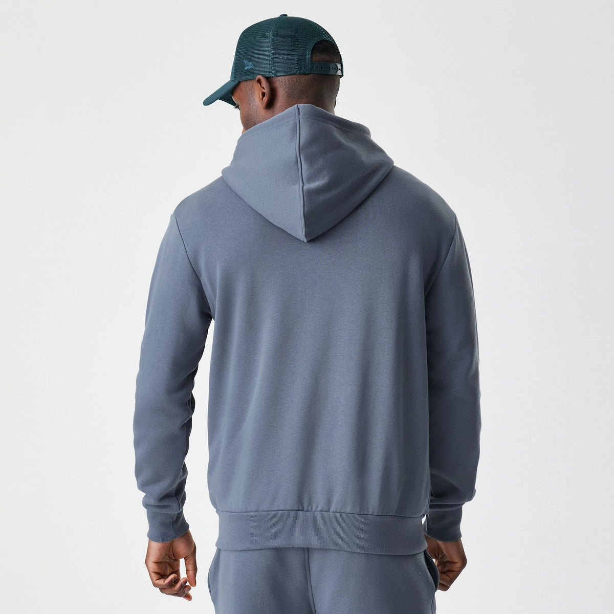 New Era LA Dodgers MLB Midi League Essential Dark Grey Full Zip Hoodie, back view showing the plain hood and ribbed hem on a model styled with a dark green cap, highlighting the hoodie’s clean and casual silhouette.