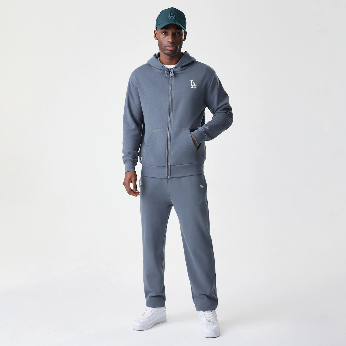 New Era LA Dodgers MLB Midi League Essential Dark Grey Full Zip Hoodie, front view on-model displaying the embroidered LA logo on the left chest, full-length zip closure and pockets, styled with matching dark grey joggers and a coordinating cap.