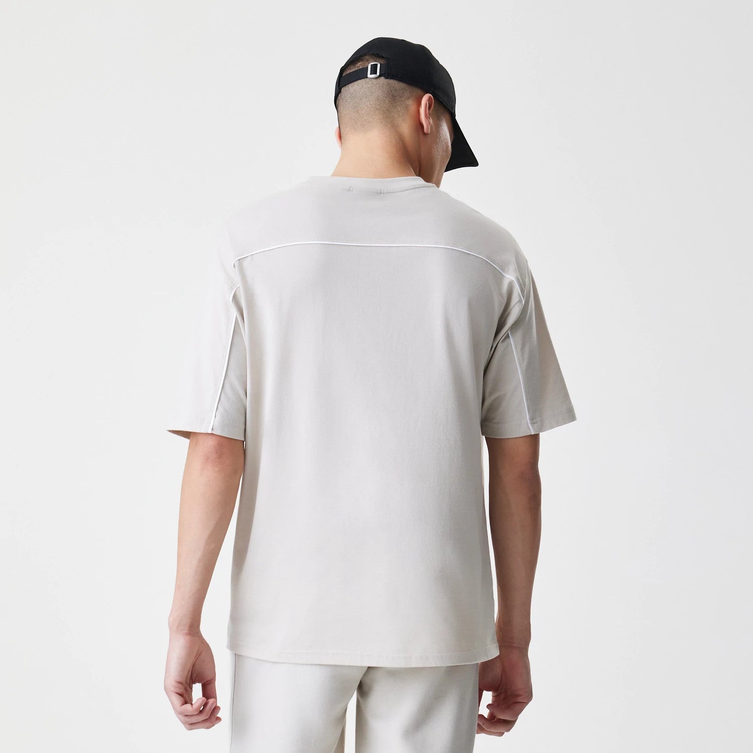 New Era LA Lakers NBA Piping Light Beige Oversized T-Shirt, back view on a model styled with light trousers and a black cap, featuring a white piping detail across the shoulders and down the sleeves.