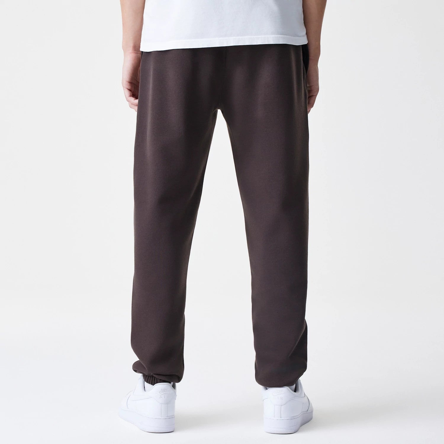 New Era New York Yankees MLB Midi League Essential Dark Brown Joggers, rear view on a model displaying the elasticated cuffs and relaxed fit, paired with white trainers and a plain white T-shirt.