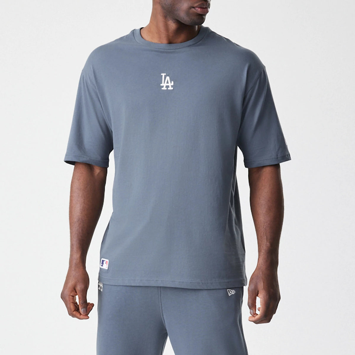New Era LA Dodgers MLB Midi League Essential Dark Grey Oversized T-Shirt, front view showing an embroidered white LA logo centred on the chest and a small New Era logo near the hem over matching dark grey trousers.