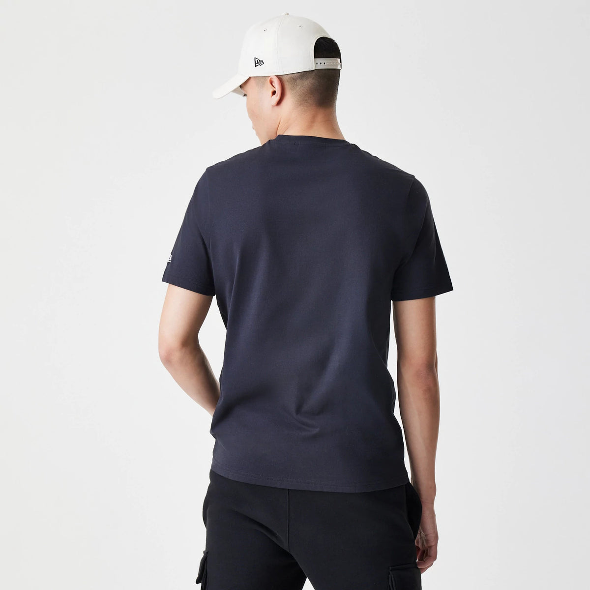 New Era New York Yankees MLB Script Graphic Navy T-Shirt, back view on a model wearing a white cap, showing the plain navy back and a small embroidered New Era logo on the left sleeve.