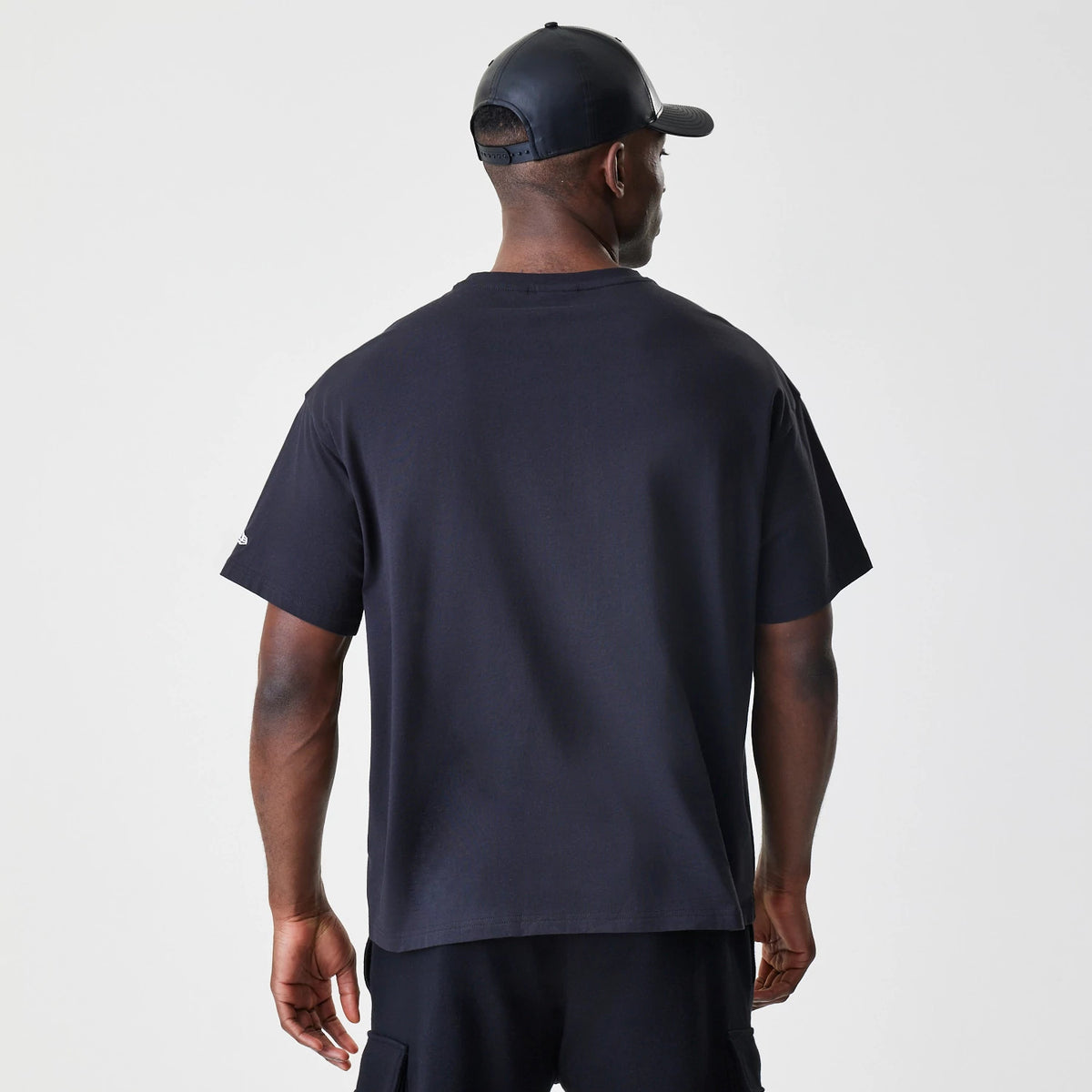 New Era LA Lakers NBA Outline Graphic Navy Oversized T-Shirt, back view on-model showing a plain navy back design with loose short sleeves, styled with a black cap completing the look.