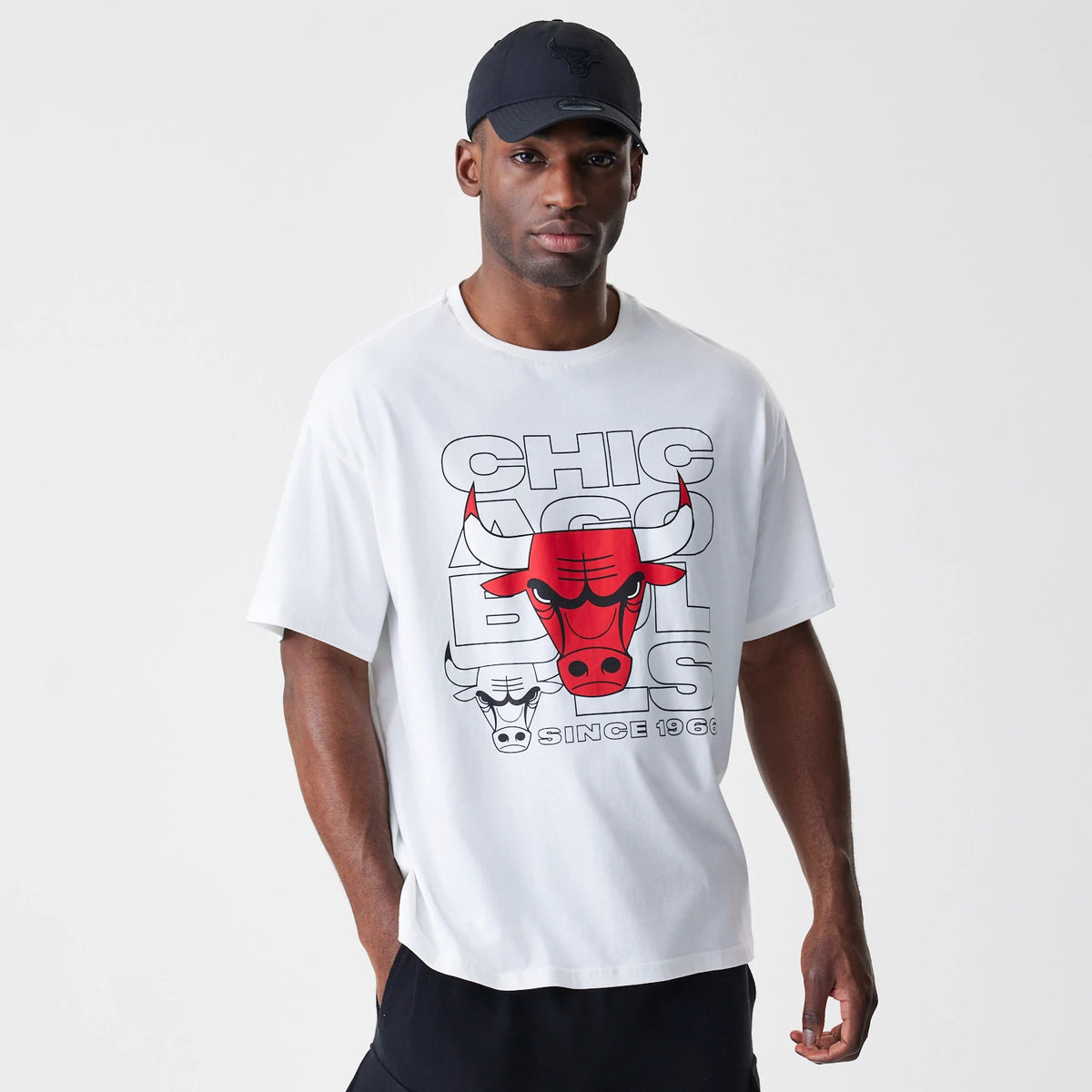 New Era Chicago Bulls NBA Outline Graphic White Oversized T-Shirt, front view on-model showing a red and black outlined Bulls logo graphic across the chest with 'Chicago Bulls Since 1966' lettering below, styled with a black cap.
