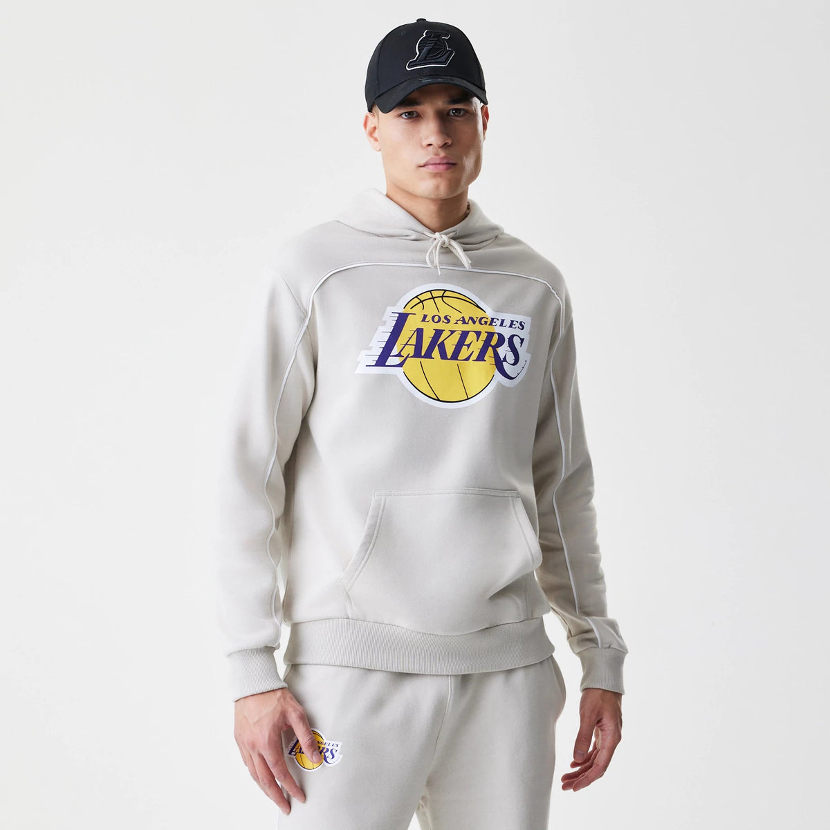 New Era LA Lakers NBA Piping Cream Oversized Pullover Hoodie, front view on-model showing the large Lakers logo emblazoned on the chest with distinctive piping detail across the shoulders and sleeves.