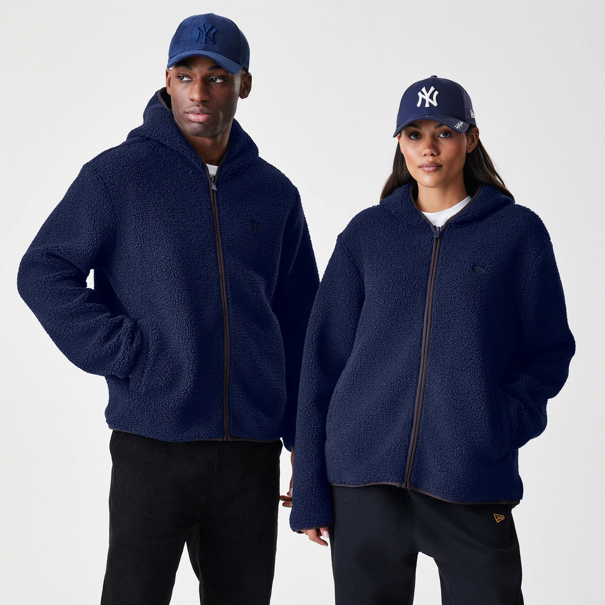 New Era Navy Hooded Sherpa Jacket, front view on models showing the deep navy textured finish with a embroidered New Era logo on the chest, a full zip closure and spacious hood, styled with matching New York Yankees caps.