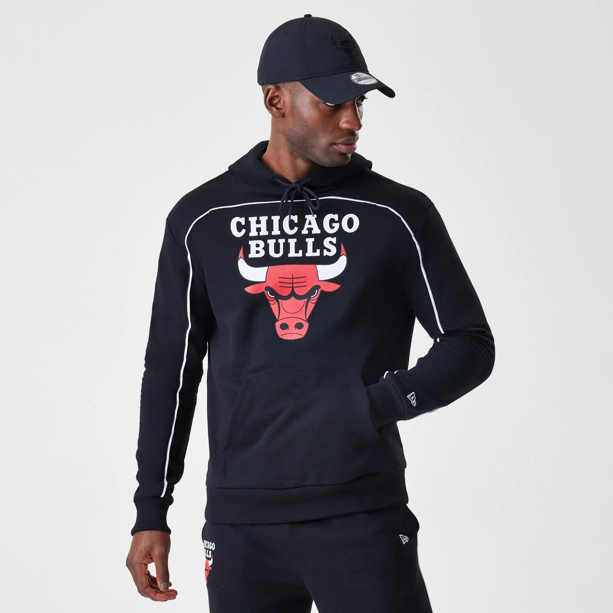 New Era Chicago Bulls NBA Piping Stripe Black Oversized Pullover Hoodie, front view on-model showing the Chicago Bulls graphic and text on the chest, with white piping along the shoulders and sleeves, and a small embroidered New Era logo on the cuff.