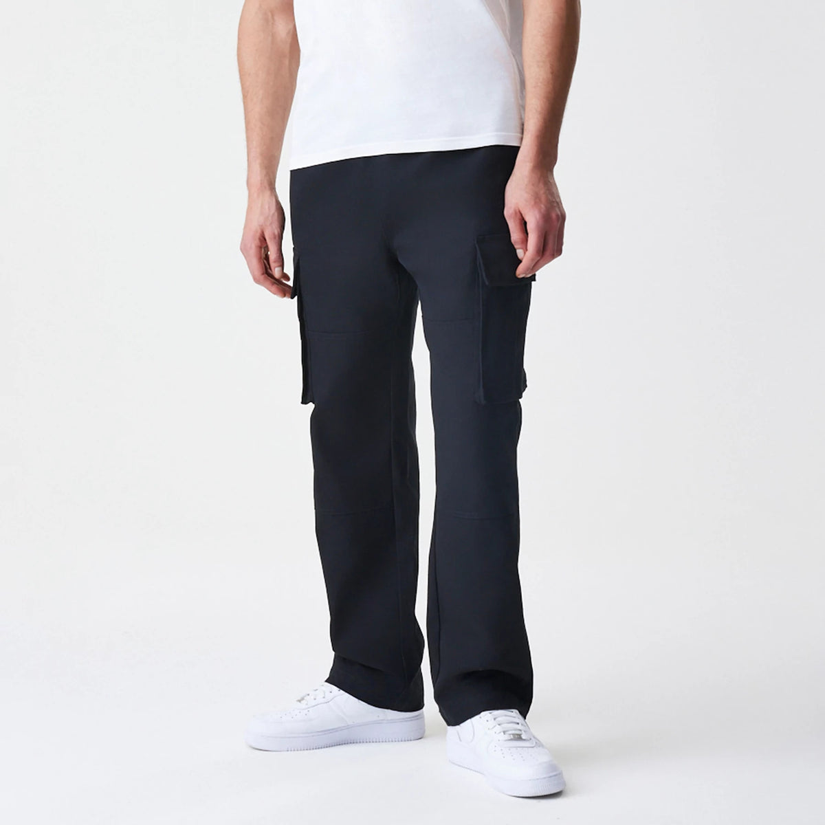 New Era Cargo Black Straight Leg Trousers, front view on a model showing large side cargo pockets and a straight leg fit, paired with a white T-shirt and white trainers for a casual look.