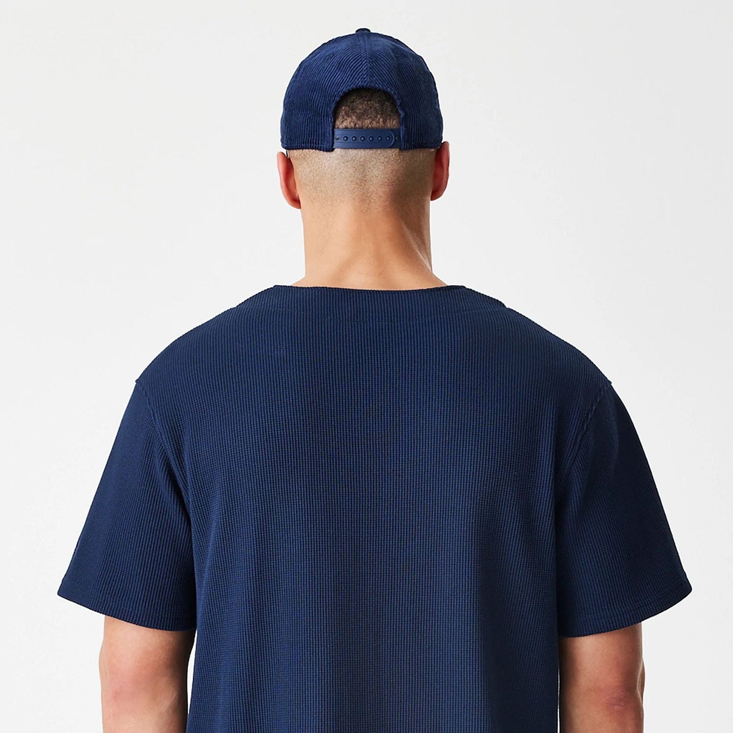 New Era Waffle Navy Jersey, back view on-model showing the textured navy fabric with a round neckline and short sleeves, contrasted by the adjustable navy strap closure of a snapback cap.
