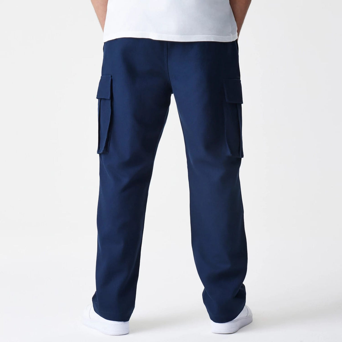 New Era Navy Straight Leg Cargo Trousers, back view on a model showing the relaxed fit with large flap pockets on each side, crafted in a deep navy fabric paired with white trainers and a white top.