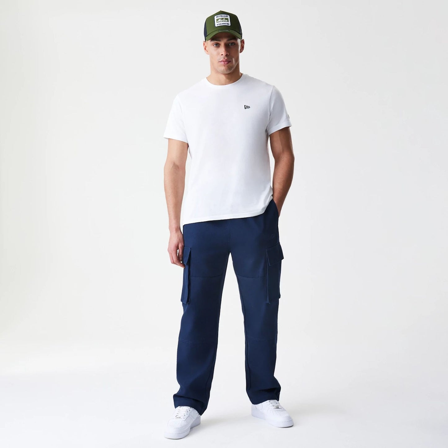 New Era Navy Straight Leg Cargo Trousers, front view on a model paired with a white T-shirt, showcasing the large side pockets and relaxed fit, complemented by a pair of white trainers.