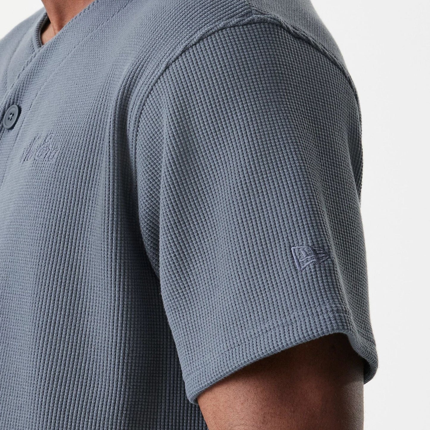New Era Waffle Dark Grey Jersey, side view on a model showing the textured waffle fabric, embroidered logo on the chest, and the New Era flag logo above the sleeve hem, with a button-up front.