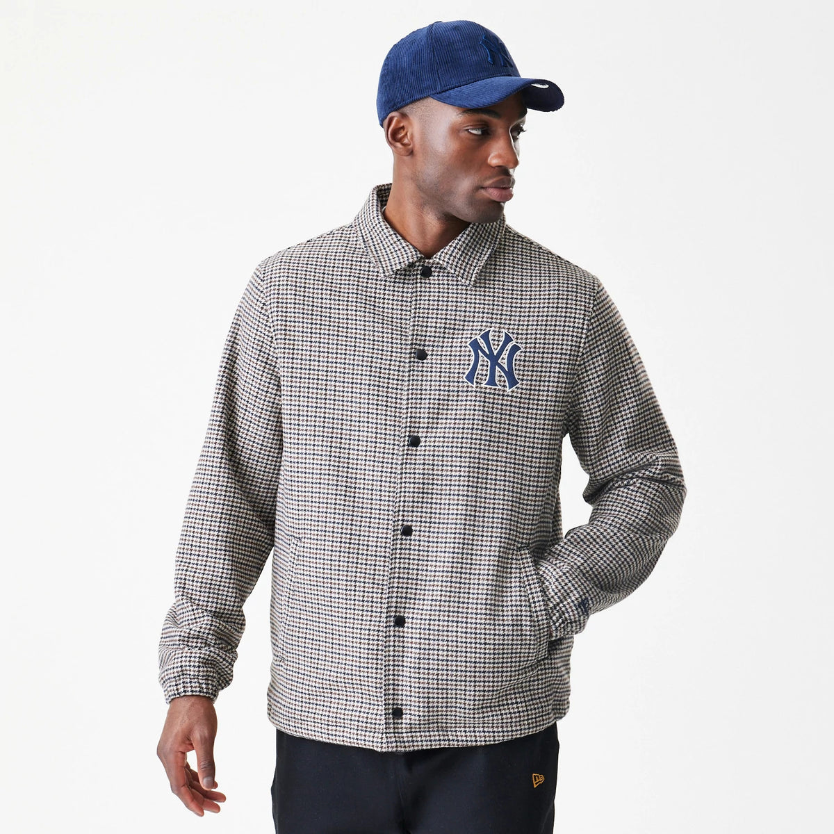 New Era New York Yankees MLB Check Brown Jacket, front view on a model wearing a blue cap, showcasing a blue embroidered Yankees logo on the left chest, black button closures down the centre, and a check pattern covering the entire jacket.