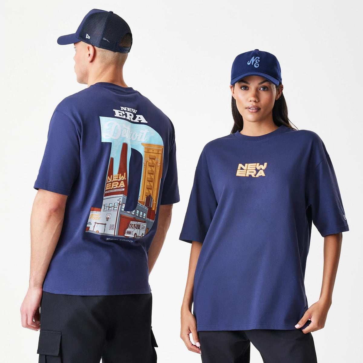 New Era Location Navy Oversized T-Shirt, front and back view on models, featuring a printed New Era logo on the front and a large Detroit graphic on the back with a skyline illustration, styled with a navy cap.