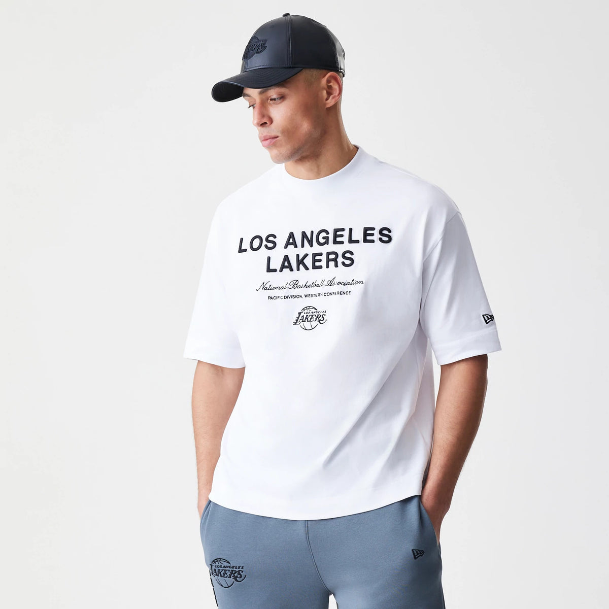 New Era LA Lakers NBA Linear White T-Shirt, front view on-model featuring black Los Angeles Lakers text across the chest, a small black Lakers logo below and an embroidered New Era logo on the left sleeve.