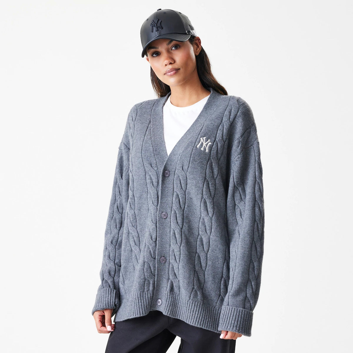 New Era New York Yankees MLB Cable Knit Dark Grey Cardigan, on a model with a black cap, featuring an embroidered white NY logo on the left chest and a textured cable knit pattern throughout the dark grey fabric.