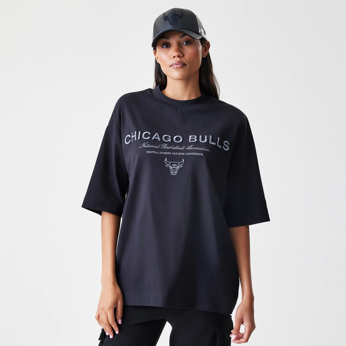 New Era Chicago Bulls NBA Linear Black T-Shirt, front view on-model showing the large embroidered CHICAGO BULLS lettering and bull logo across the chest, styled with a matching black cap featuring an embroidered front logo.