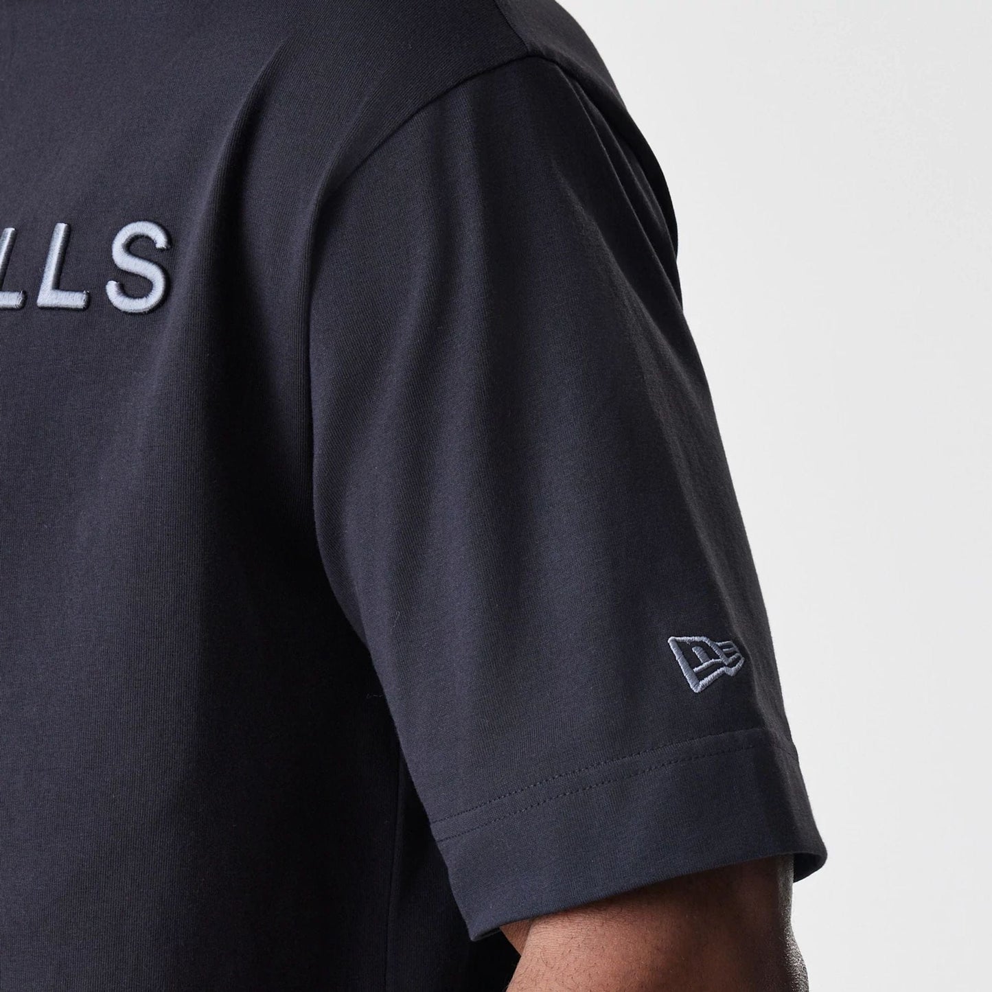 New Era Chicago Bulls NBA Linear Black T-Shirt, side view capturing the white embroidered Bulls lettering across the chest and a small white embroidered New Era logo on the sleeve, showing the T-shirt's black fabric.