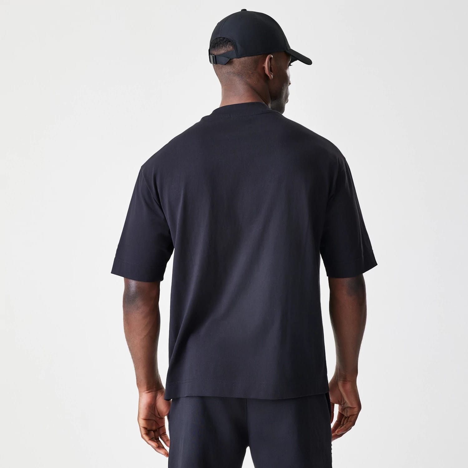 New Era Chicago Bulls NBA Linear Black T-Shirt, back view on a model styled with a black cap, showing the plain black fabric of the shirt and the loose fit extending past the waist.