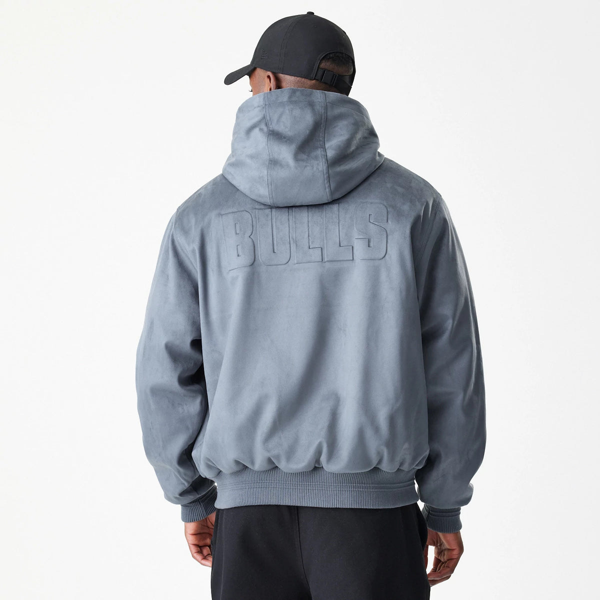New Era Chicago Bulls NBA Suede Dark Grey Jacket, back view on-model showing the hood and large raised Bulls lettering across the upper back, with ribbed cuffs and hem complementing the dark grey finish.