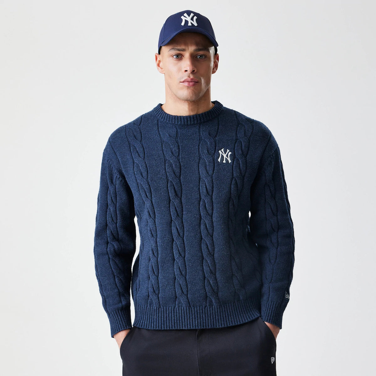 New Era New York Yankees MLB Cable Knit Navy Knitted Sweater, front view on a model showing the white Yankees logo embroidered on the left chest, with prominent cable knit and a ribbed crew neck.
