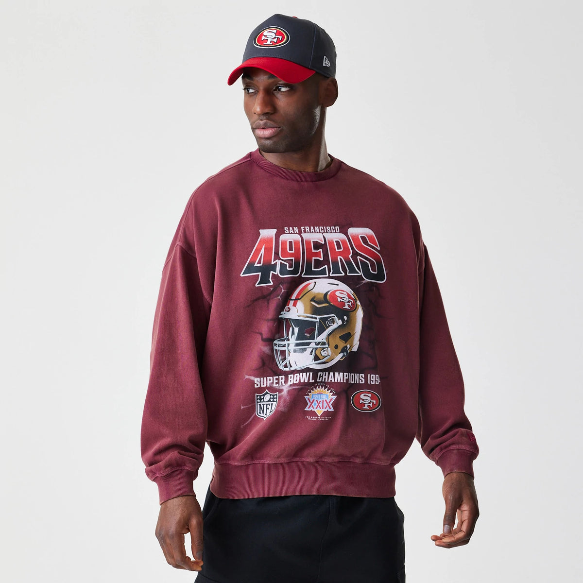 New Era San Francisco 49ers NFL Washed Boxy Dark Red Oversized Crew Neck Sweater, front view on a model with a matching cap, features a large 49ers graphic and helmet print across the chest, celebrating Super Bowl champions.