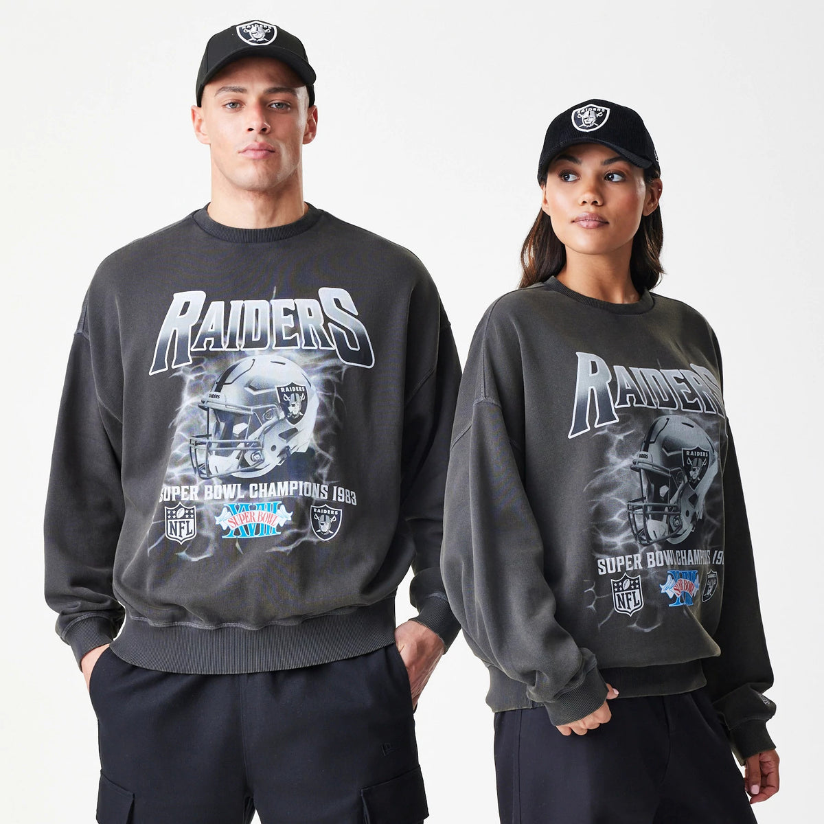 New Era Las Vegas Raiders NFL Washed Boxy Dark Grey Oversized Crew Neck Sweater, front view on models showing large Raiders helmet graphic with Super Bowl Champions 1983 text and team logos across the chest.