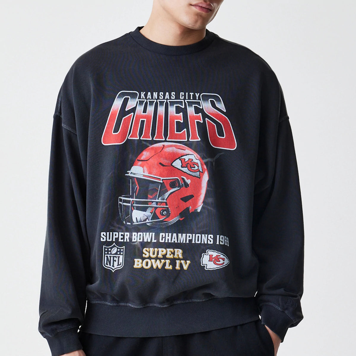 New Era Kansas City Chiefs NFL Washed Boxy Black Oversized Crew Neck Sweater, front view on a model showing large Chiefs lettering above a red helmet graphic with Super Bowl Champions 1969 and Super Bowl IV details.