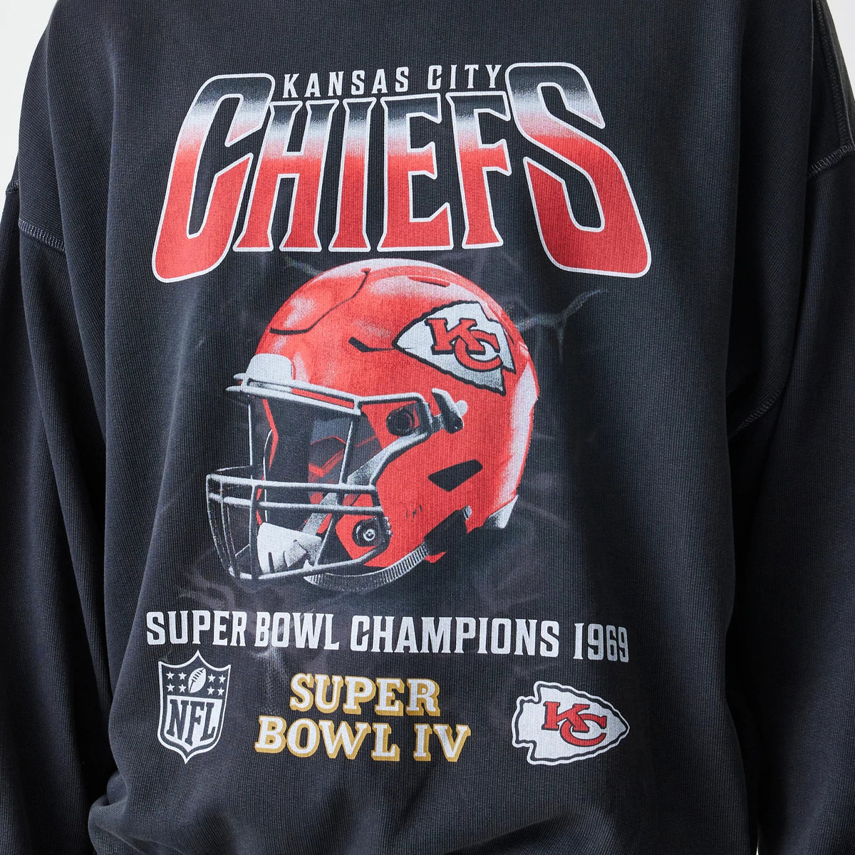 New Era Kansas City Chiefs NFL Washed Boxy Black Oversized Crew Neck Sweater, front view showing a large graphic with Kansas City Chiefs lettering, a red helmet image, Super Bowl Champions 1969 text, and NFL and team logos.