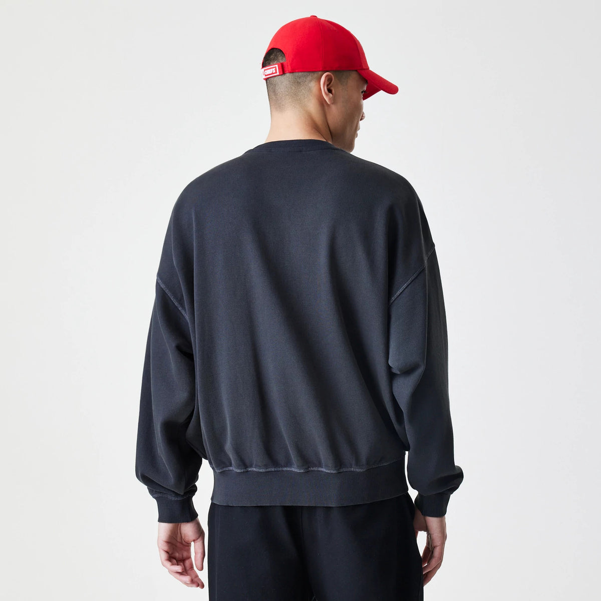 New Era Kansas City Chiefs NFL Washed Boxy Black Oversized Crew Neck Sweater, back view on a model wearing a red cap, showing the dropped shoulder seams and ribbed hem and cuffs of the relaxed fit design.