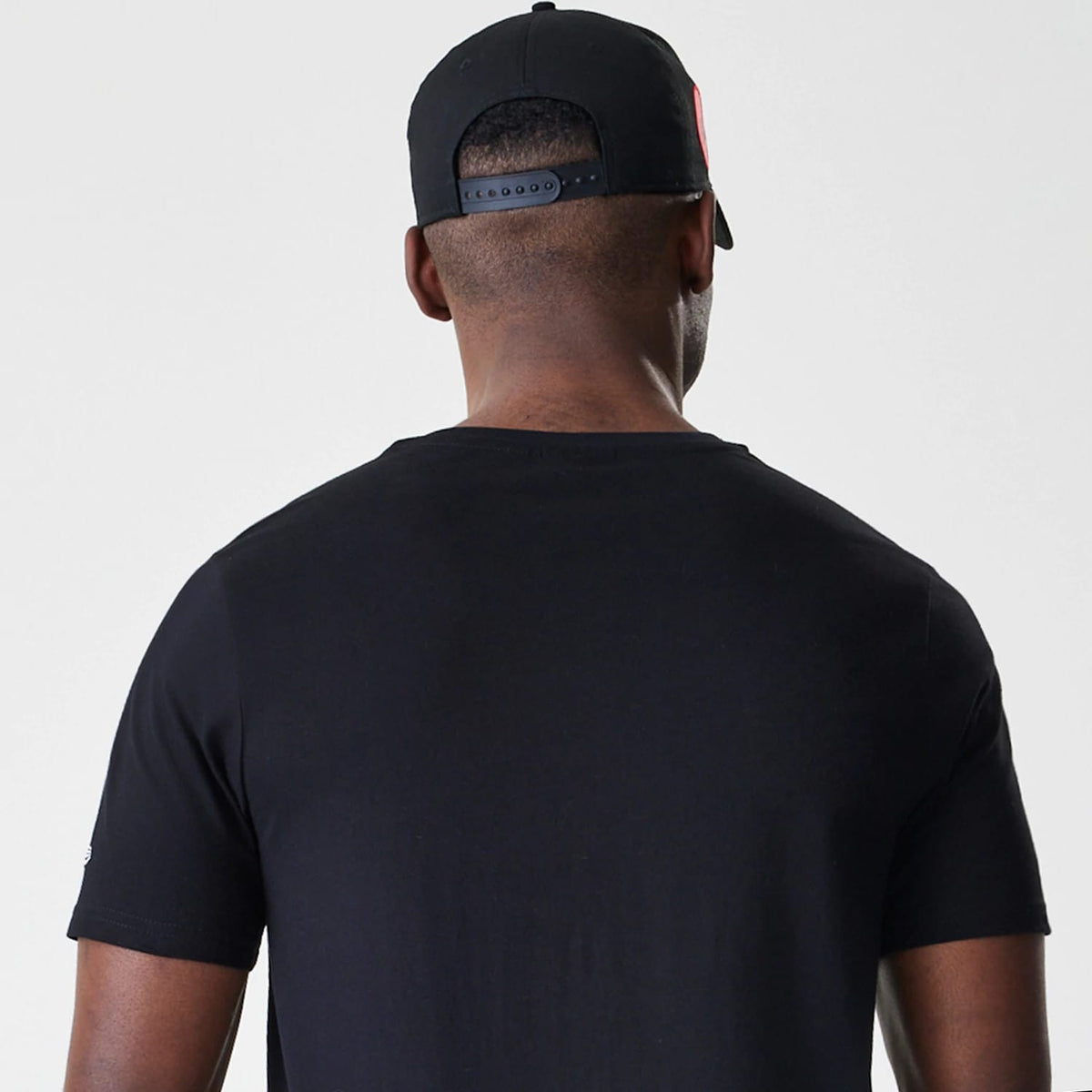 New Era Chicago Bulls NBA Script Black T-Shirt, back view on-model showing the plain black design with a crew neck collar, paired with a black cap featuring a snapback closure and embroidered detail on the front.