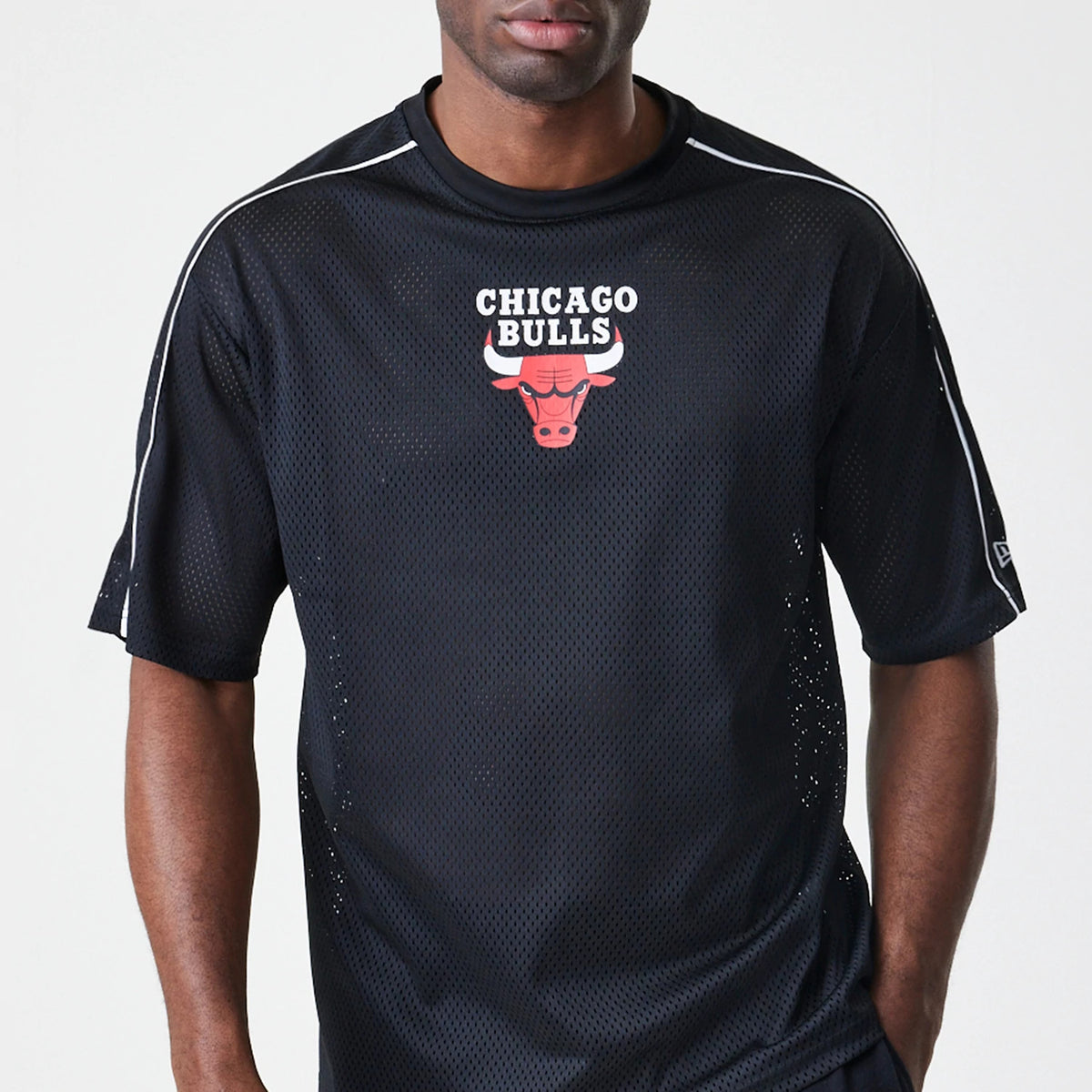 New Era Chicago Bulls NBA Piping Black Oversized T-Shirt, front view on a model showing the Chicago Bulls logo with red embroidered details on the chest, white piping along the shoulders, and a small embroidered New Era logo on the sleeve edge.