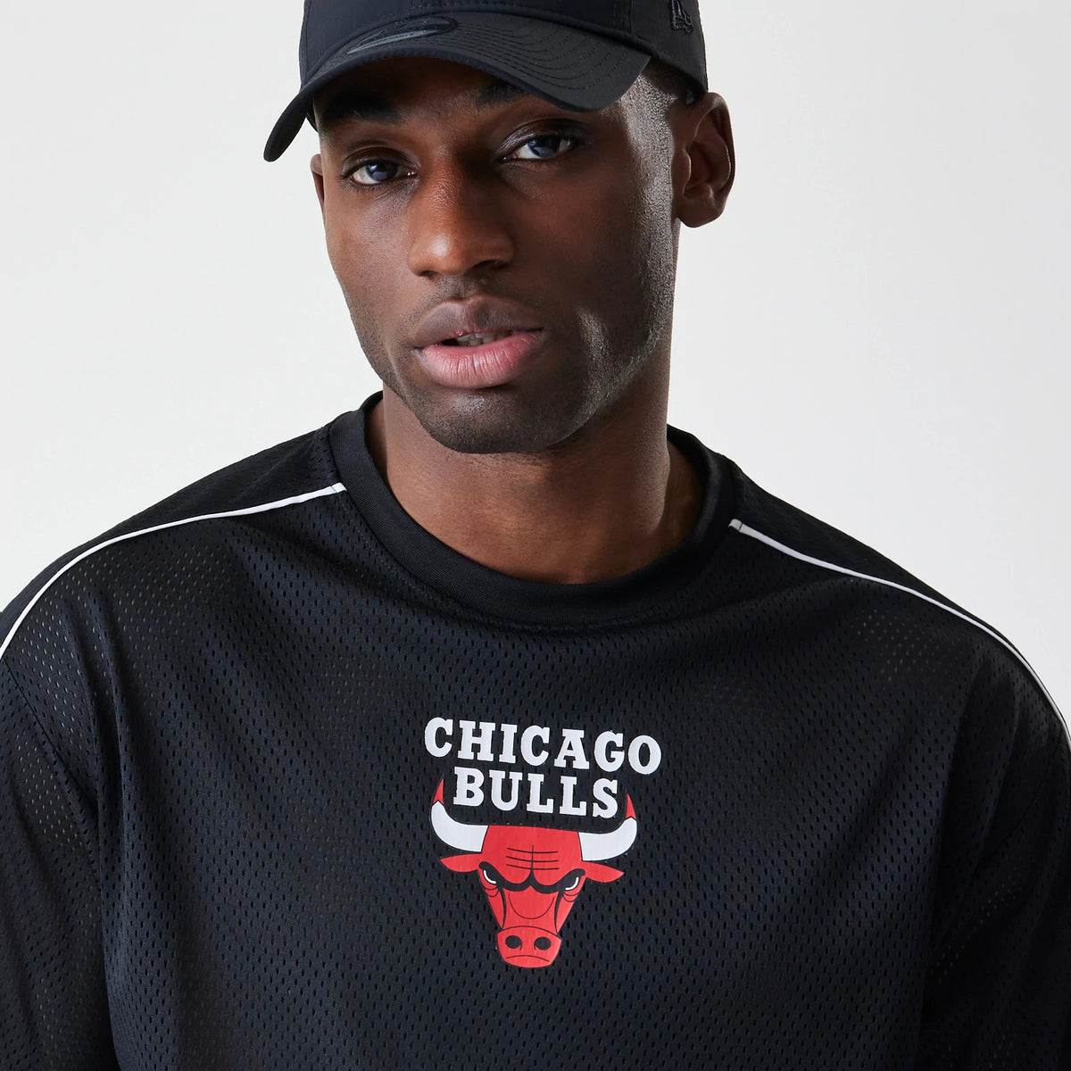 New Era Chicago Bulls NBA Piping Black Oversized T-Shirt, front view on-model showing the printed Chicago Bulls logo and lettering on the chest, with white piping along the shoulders, paired with a black cap.