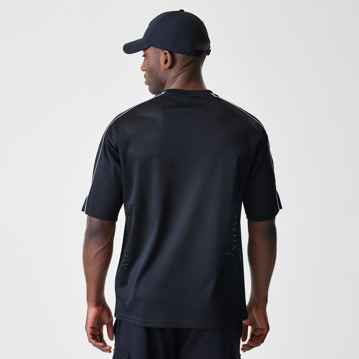 New Era Chicago Bulls NBA Piping Black Oversized T-Shirt, back view showing the plain black mesh fabric with vertical piping along the shoulders, worn by a model with a matching black cap and shorts.