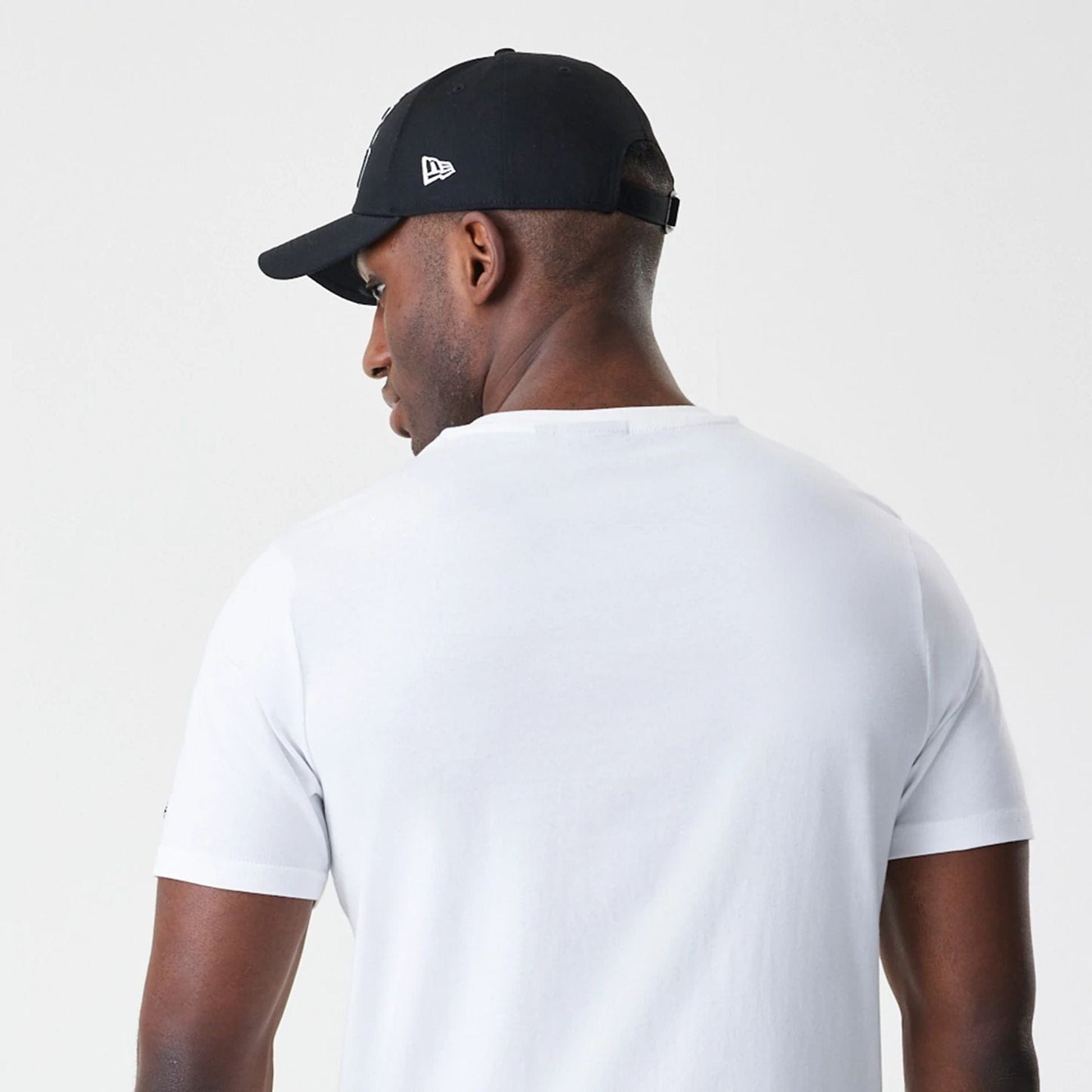 New Era LA Lakers NBA Script White T-Shirt, back view on a model with a black cap, showing the plain white fabric of the T-shirt and the cap featuring a raised New Era logo on the side.