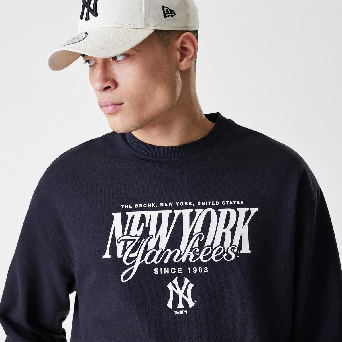 New Era New York Yankees MLB Script Black Crew Neck Sweater, front view on a model wearing a light cap, featuring white New York Yankees lettering across the chest and an embroidered team logo beneath.