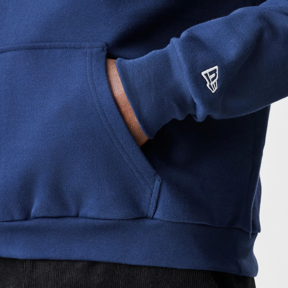 New Era New York Yankees MLB Script Navy Oversized Pullover Hoodie, three-quarter view showing the front pocket with a hand inside and a white embroidered New Era logo on the sleeve cuff.