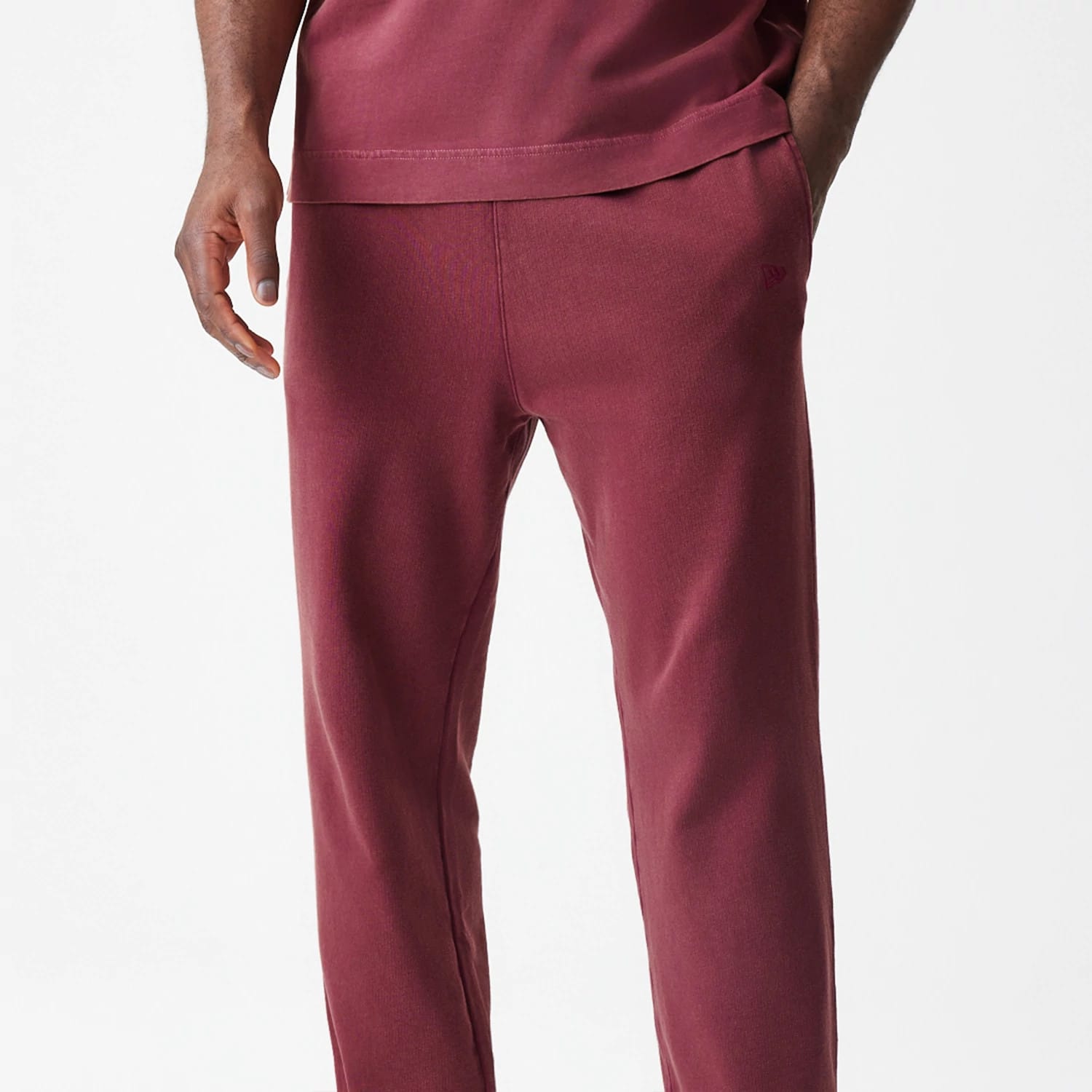 New Era Washed Dark Red Straight Leg Joggers, front view on a model showing side pockets and a embroidered New Era flag logo on the left hip, with a relaxed fit cut and a comfortable waistband.