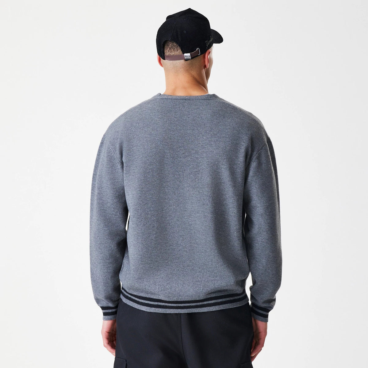 New Era Dark Grey Cardigan, rear view on a model showing a plain back with ribbed cuffs and striped waistband in dark and light grey, worn over black trousers.