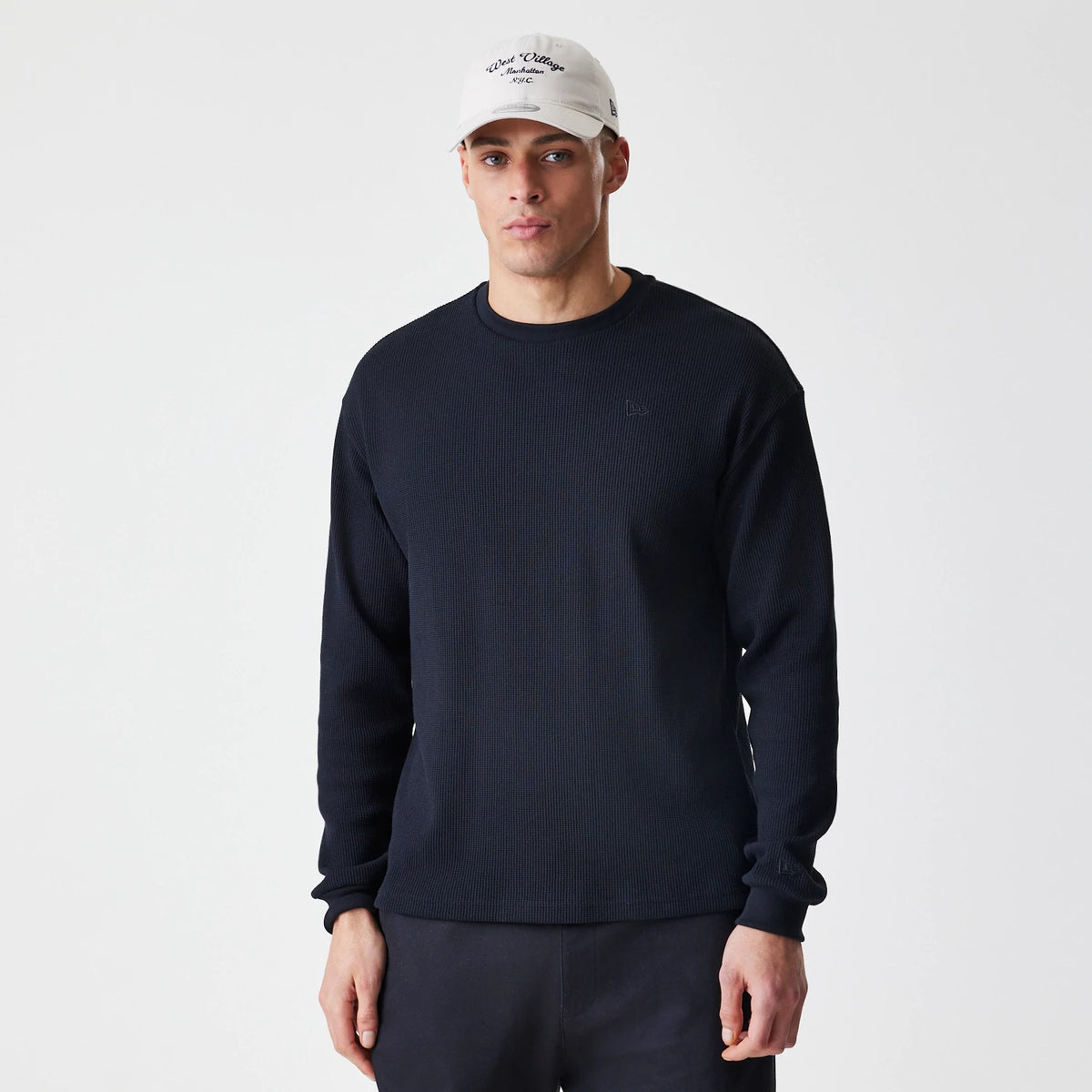 New Era Waffle Black Long Sleeve T-Shirt, front view on a model with a white cap, featuring a embroidered New Era logo on the chest and ribbed cuffs, illustrating a relaxed fit and classic crew neck design.