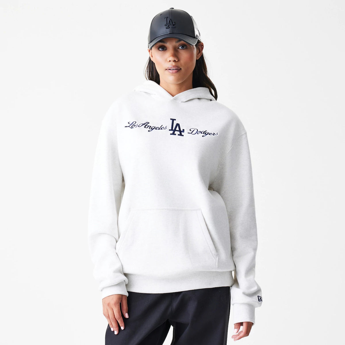 New Era LA Dodgers MLB Script White Oversized Pullover Hoodie, front view on a model wearing a matching cap, showing navy embroidered script lettering across the chest and a New Era logo on the left cuff above a kangaroo pocket.
