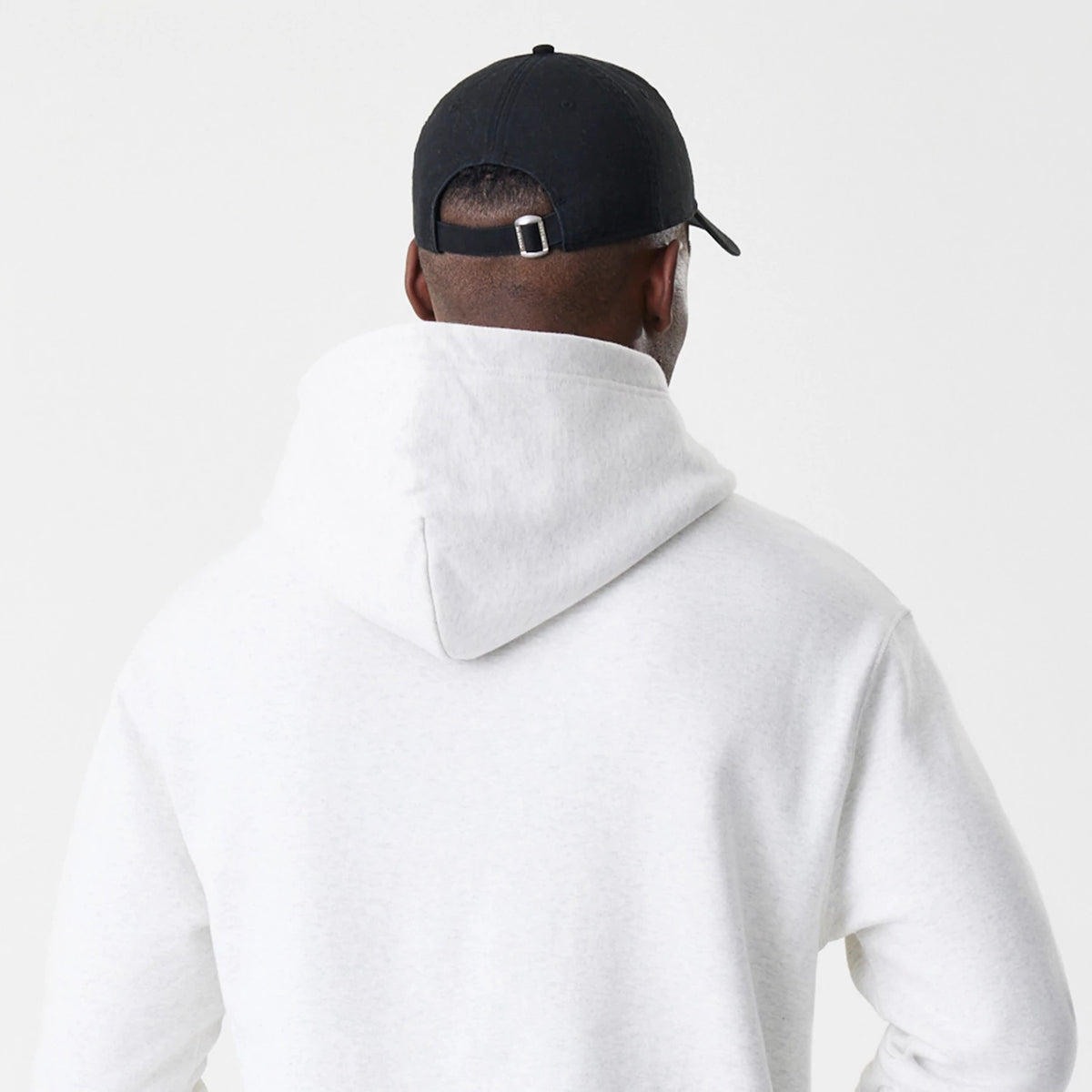 New Era LA Dodgers MLB Script White Oversized Pullover Hoodie, back view on a model showing the large hood resting flat and the relaxed fit, paired with a black cap featuring a buckle strap at the back.