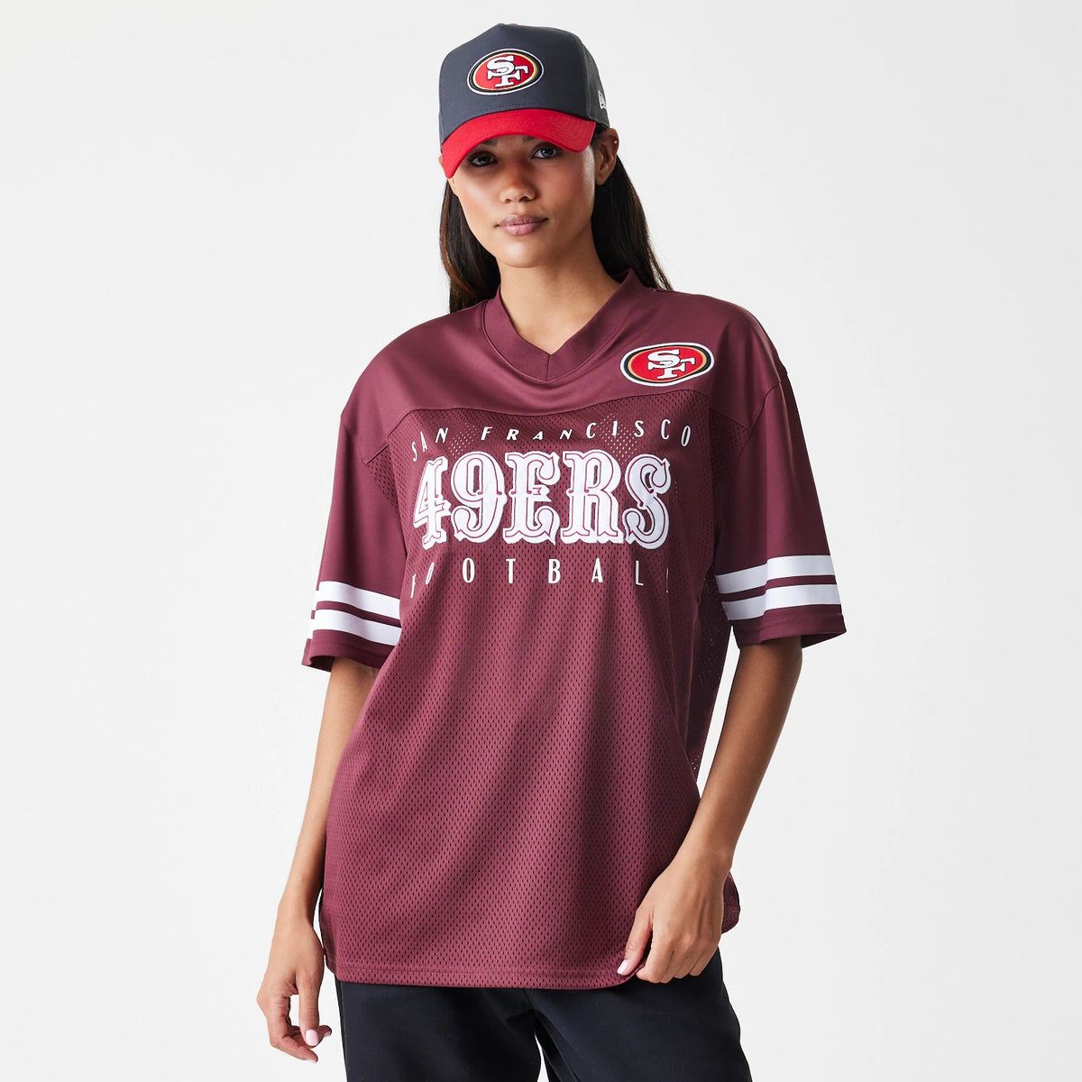 New Era San Francisco 49ers NFL Mesh Dark Red Jersey, front view on a model with a grey and red cap, featuring large white 49ERS lettering across the chest and a 49ers logo patch on the right shoulder, with striped sleeves.