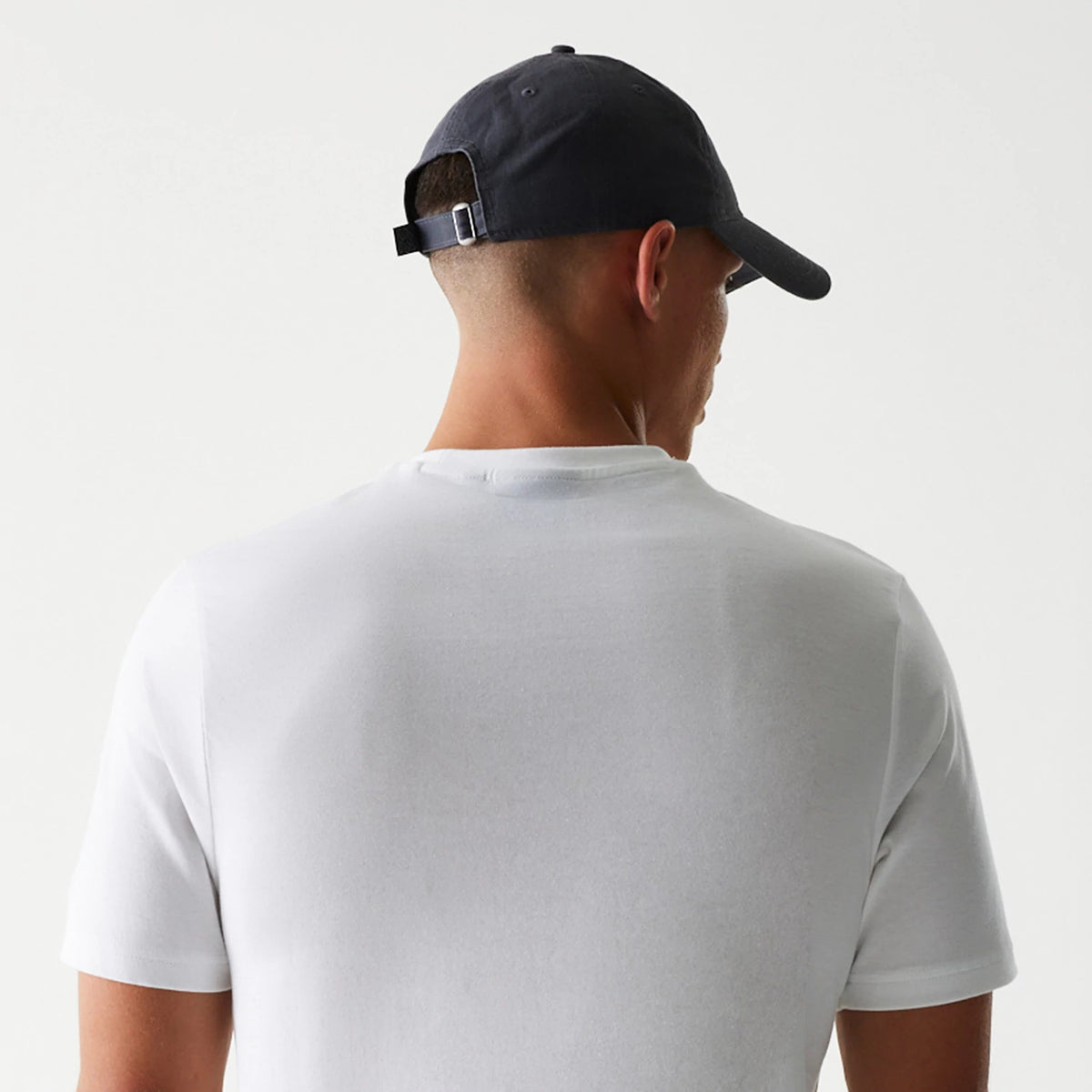 New Era New York Yankees MLB Baseball Graphic White T-Shirt, back view on-model showing the plain white fabric extending across the shoulders and down to the short sleeves, paired with a dark cap featuring an adjustable strap at the back.