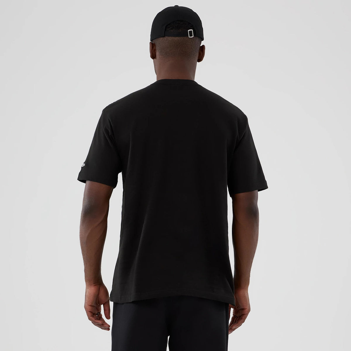 New Era Friends Turkey Head Lifestyle Graphic Black T-Shirt, back view on a model wearing a matching black cap, displaying plain black back with short sleeves and an embroidered logo on the left sleeve.