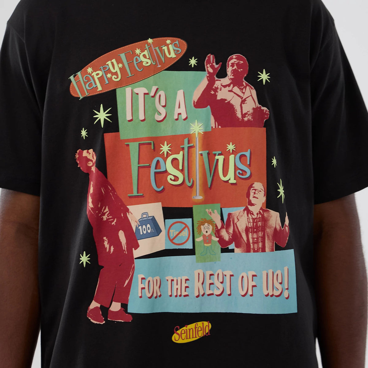 New Era Seinfeld Lifestyle Graphic Black T-Shirt, front view on a model featuring a colourful collage of Festivus-themed graphics and text including Happy Festivus and For the Rest of Us! with a small yellow Seinfeld logo at the bottom.