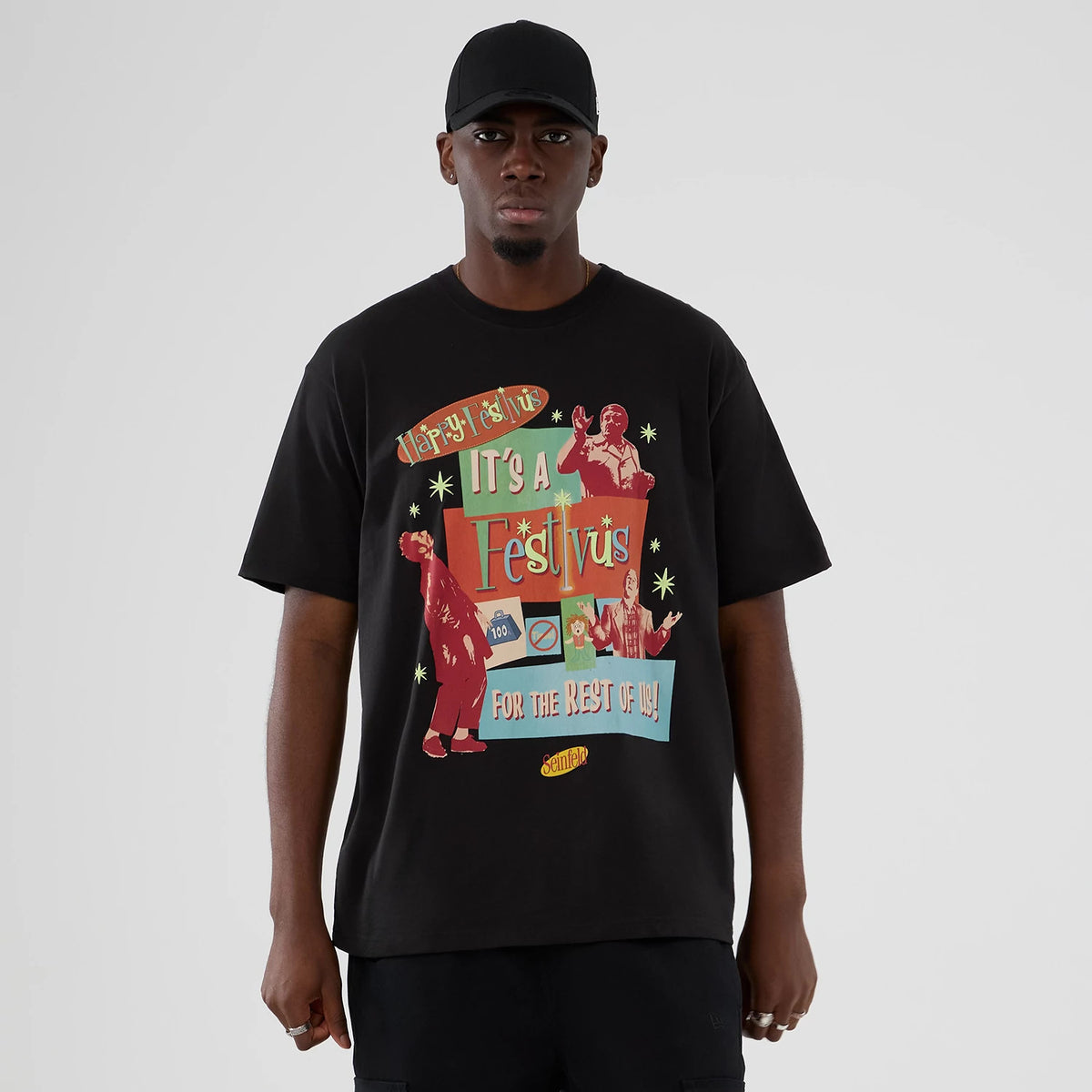 New Era Seinfeld Lifestyle Graphic Black T-Shirt, front view on-model featuring a graphic with It's a Festivus for the Rest of Us! in colourful text, retro illustrations of characters, and the Seinfeld logo at the bottom.