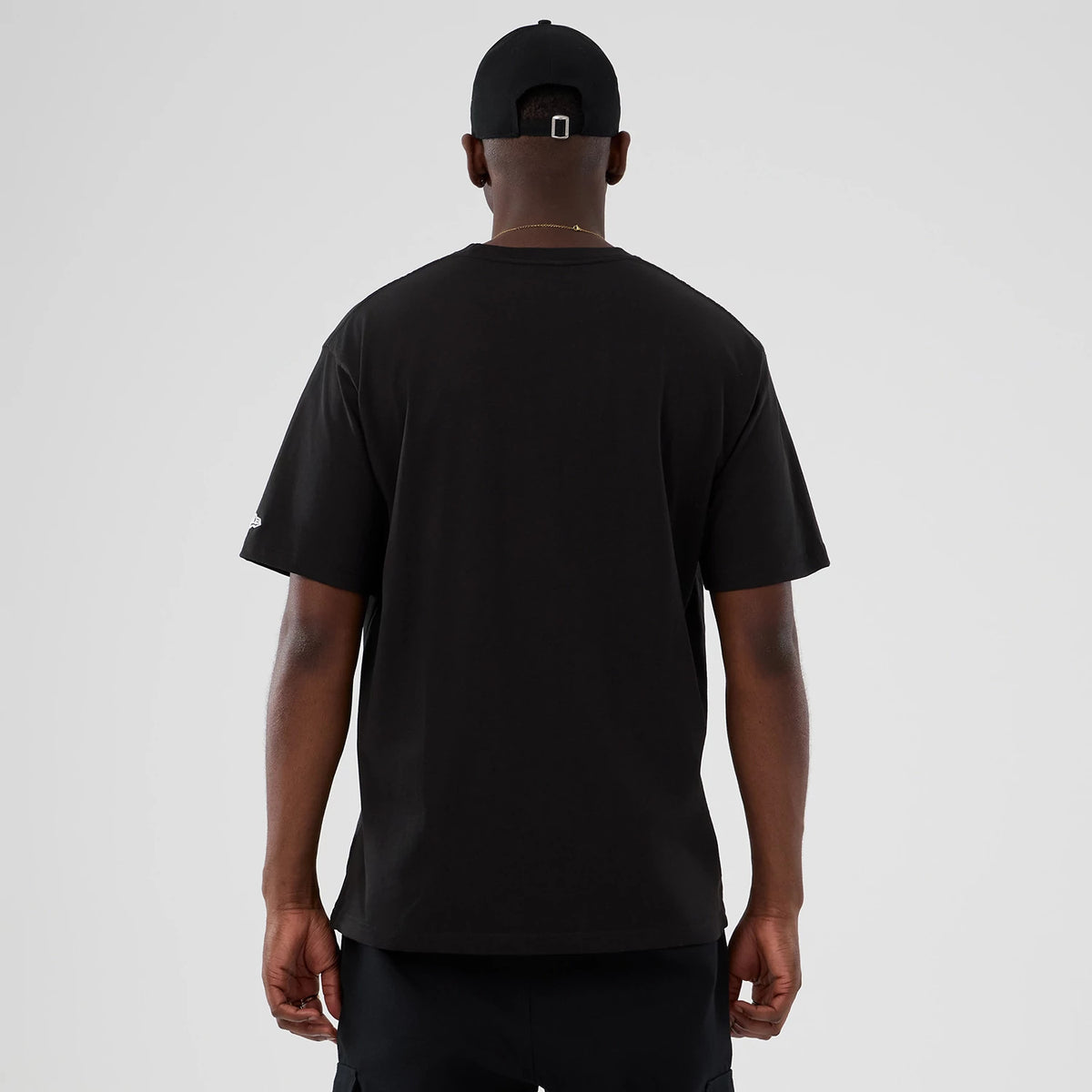 New Era Seinfeld Lifestyle Graphic Black T-Shirt, back view on a model with a plain black cap, showing a solid black back with short sleeves and no graphics or text, highlighting the shirt's minimalist design.