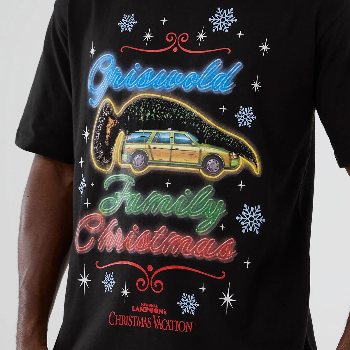 New Era National Lampoon's Christmas Vacation Lifestyle Graphic Black T-Shirt, front view showing a design with a car, Christmas tree, and Griswold Family Christmas text in neon-style colours, surrounded by snowflakes on the black fabric.