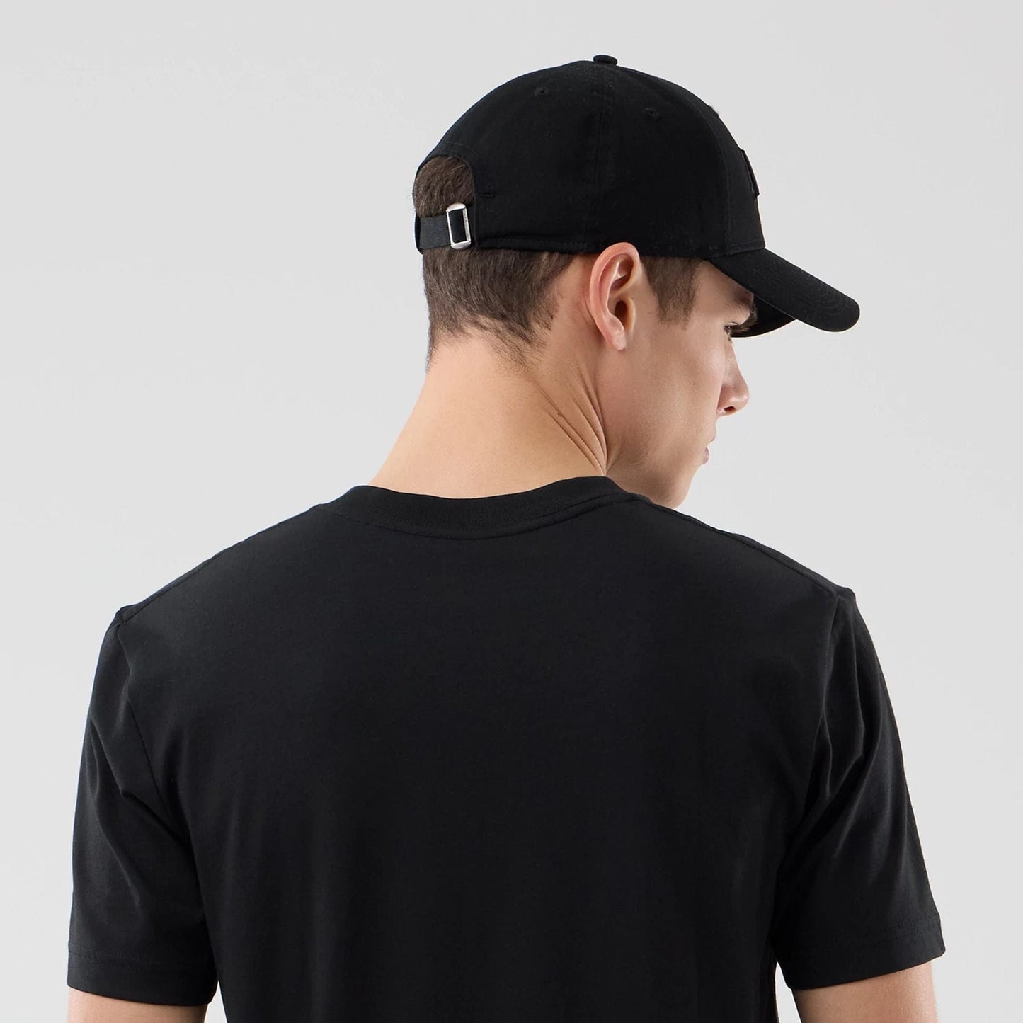 New Era LA Lakers NBA City Edition Black T-Shirt, back view on-model showing plain black fabric from the shoulders down, with a black cap featuring an adjustable strap and small buckle at the back of the head.